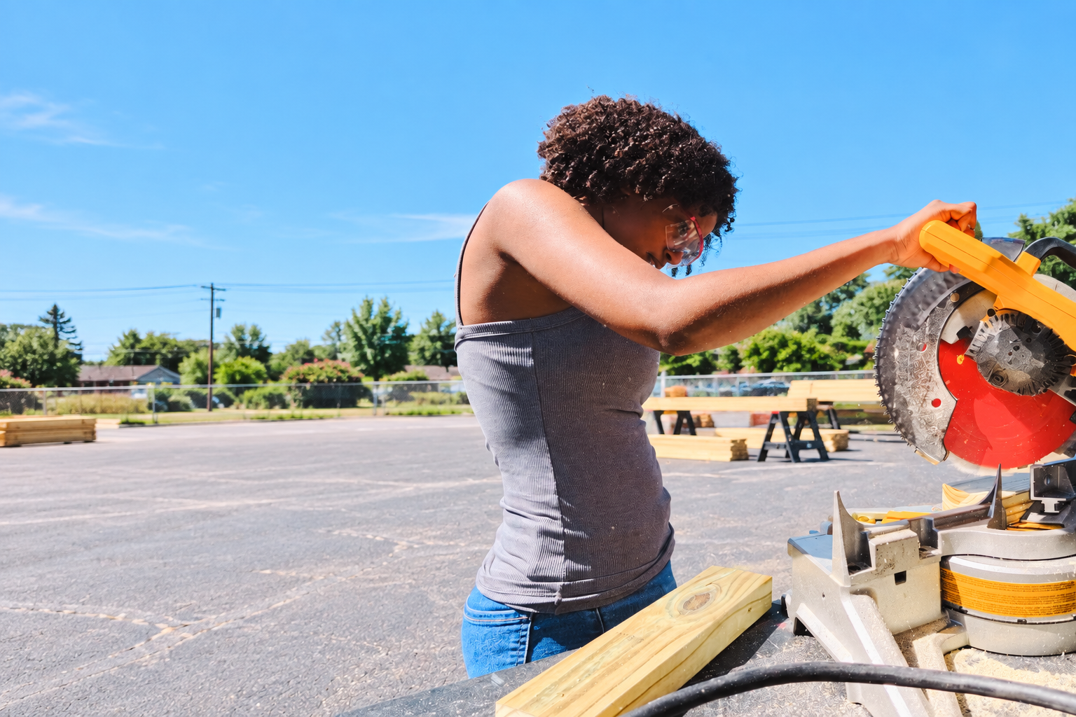 A young woman wearing safety glasses uses a miter saw at Kids Construction Camp